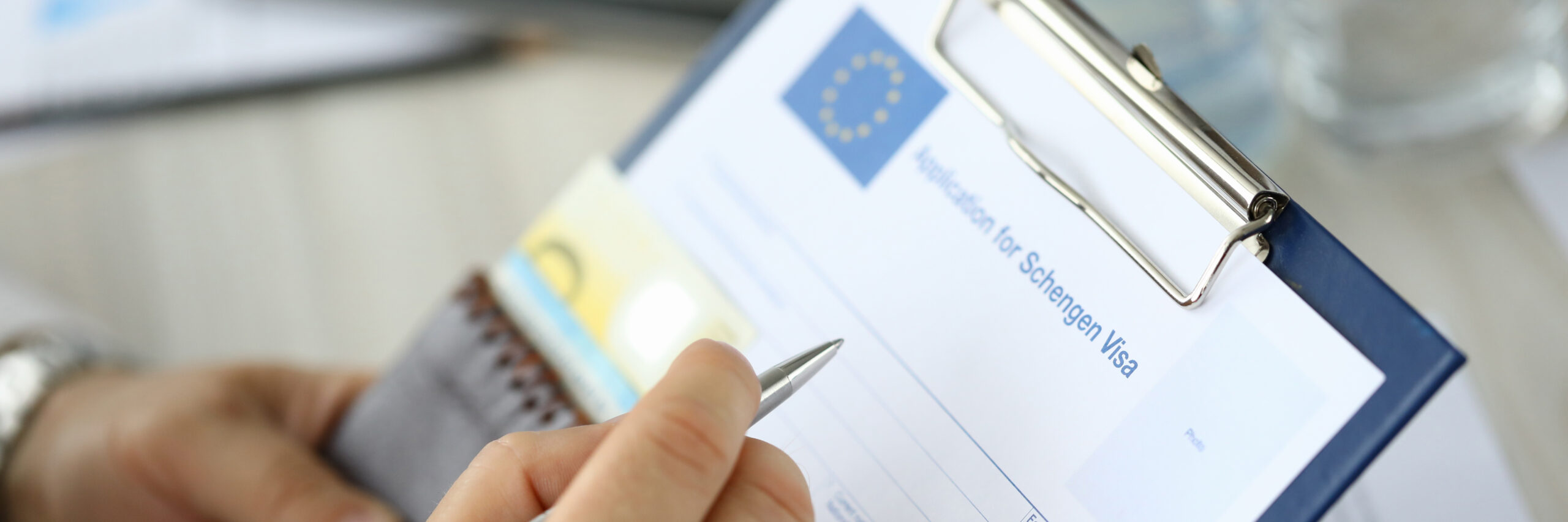 Close-up of person filling application form for schengen visa on clipboard. Man holding silver pen. Writing personal information on paper. Travelling abroad or immigration concept